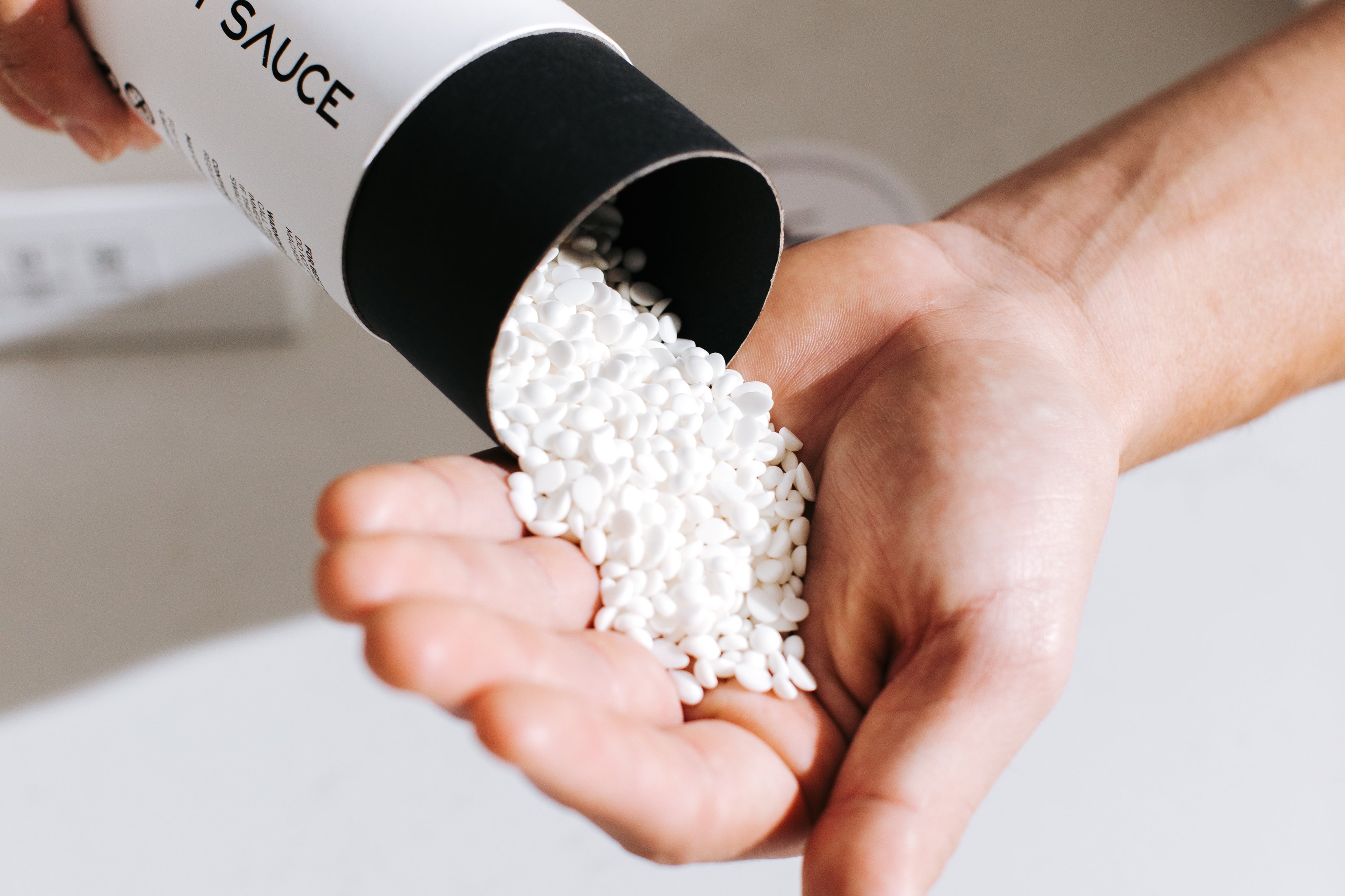 Hand pouring white Laundry Sauce Laundry Scent Booster beads from the canister into a palm