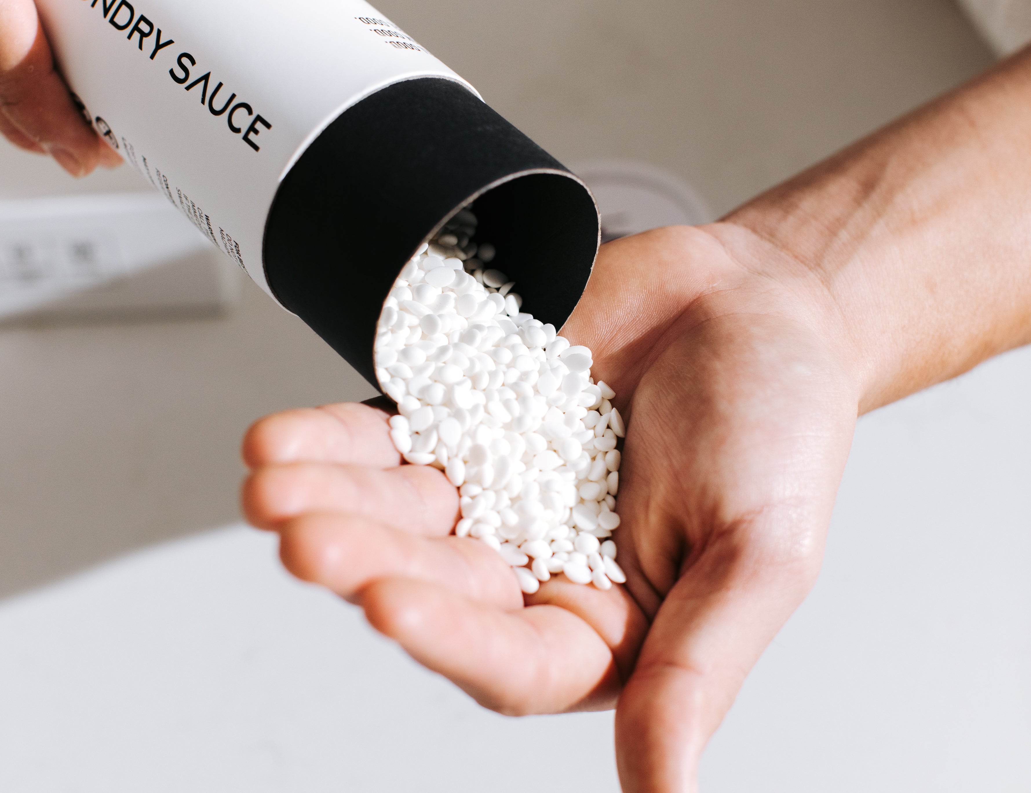Hand pouring white Laundry Sauce Laundry Scent Booster beads from the canister into a palm