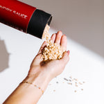 Hand pouring peach Laundry Sauce Laundry Scent Booster beads from a red canister