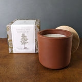 Los Poblanos Herbal Bug Repellent candle in a terracotta pot with its printed box on a leather surface