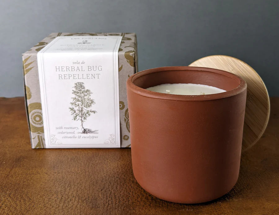Los Poblanos Herbal Bug Repellent candle in a terracotta pot with its printed box on a leather surface