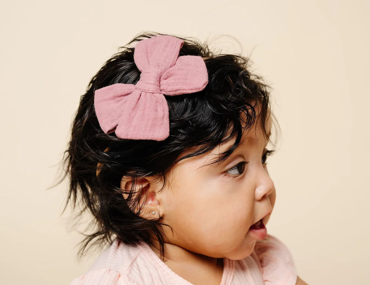 Lou Lou & Company Adventure Bow in mauve pink worn by a baby girl with dark curls in a pink top