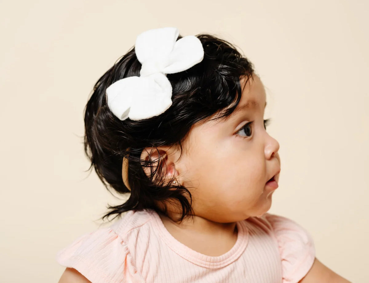 Lou Lou & Company Adventure Bow in white worn by a baby girl with dark curls in a pink top