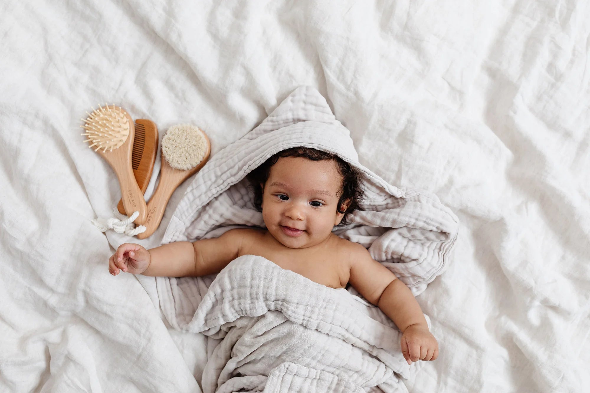 Lou Lou & Company Baby Hair Brush Set, a smiling baby in a hooded towel next to the wooden brushes