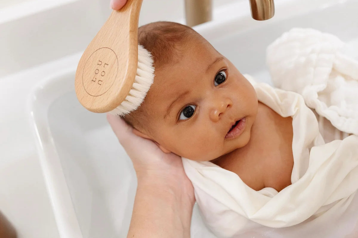 Lou Lou & Company Baby Hair Brush Set, a baby wrapped in a towel being brushed at the sink
