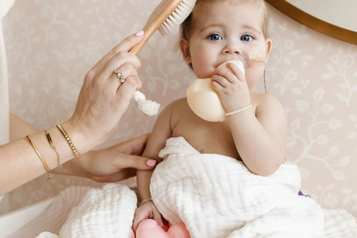 Lou Lou & Company Baby Hair Brush Set, a baby in a white towel having their hair brushed with the wooden brush
