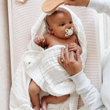 Lou Lou & Company Baby Hair Brush Set, a newborn with a pacifier having their hair brushed in a striped crib