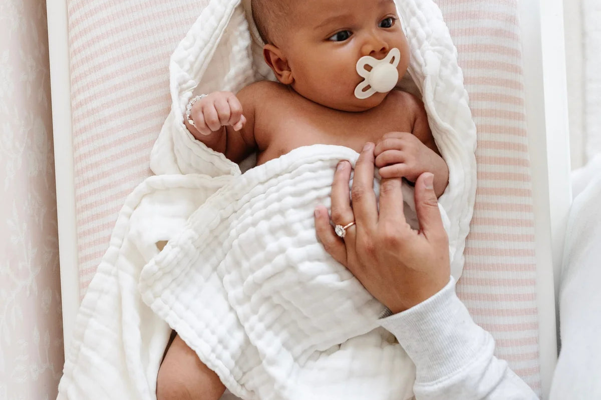 Lou Lou & Company Baby Hair Brush Set, a newborn in a white blanket being brushed in a crib