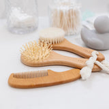 Lou Lou & Company Baby Hair Brush Set, wooden brushes and comb on a bathroom counter beside jars of cotton swabs