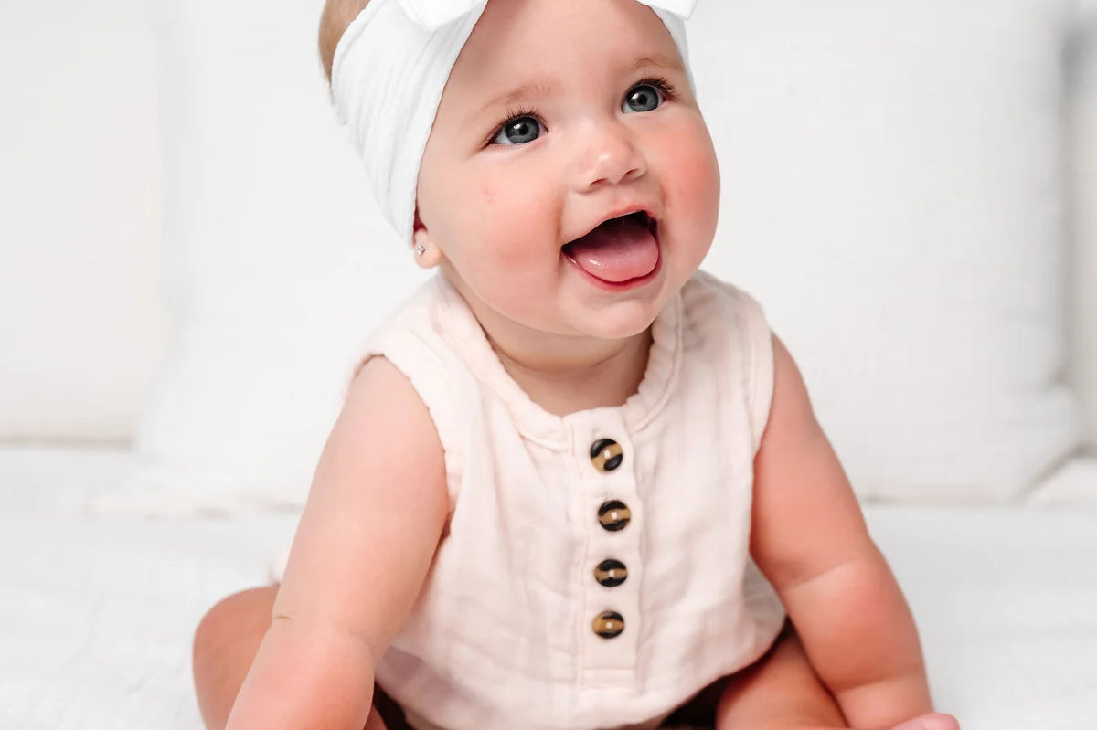 Laughing baby in a blush romper wearing the Lou Lou & Company Cable Knit Headband in Crystal White