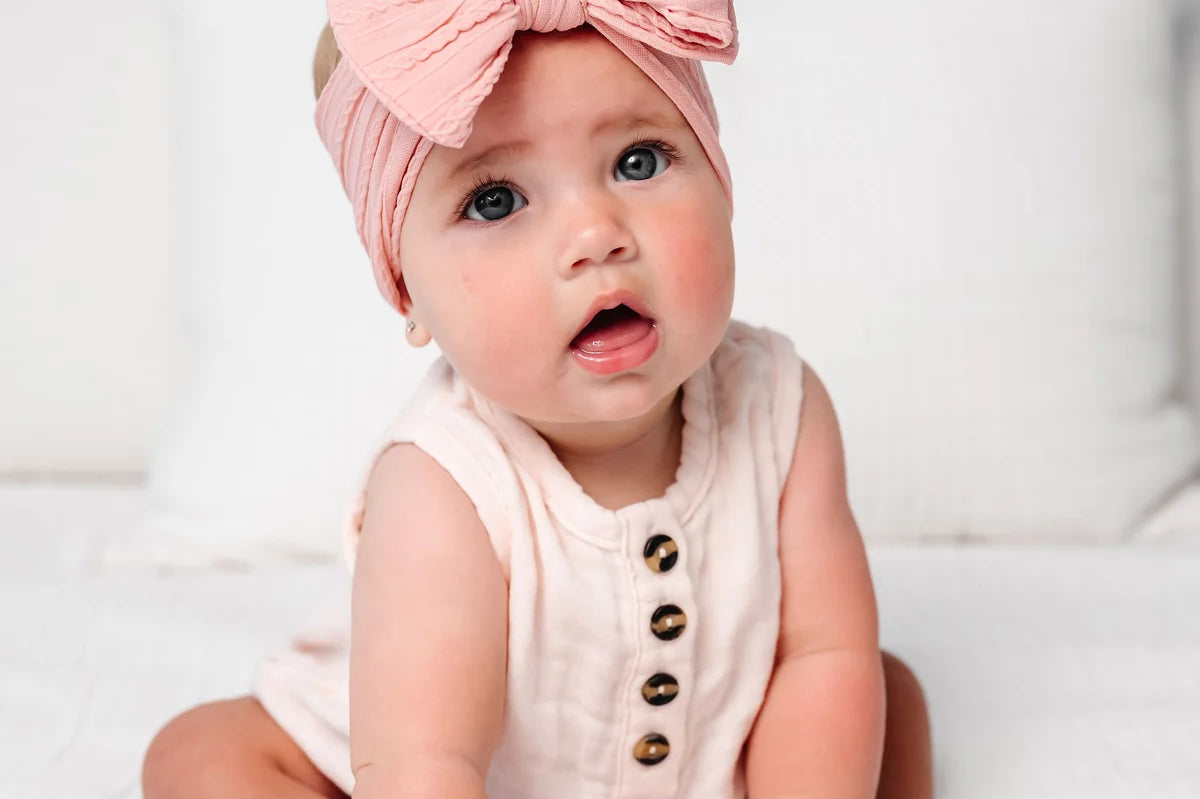Baby in a blush romper wearing the Lou Lou & Company Cable Knit Headband in Rose