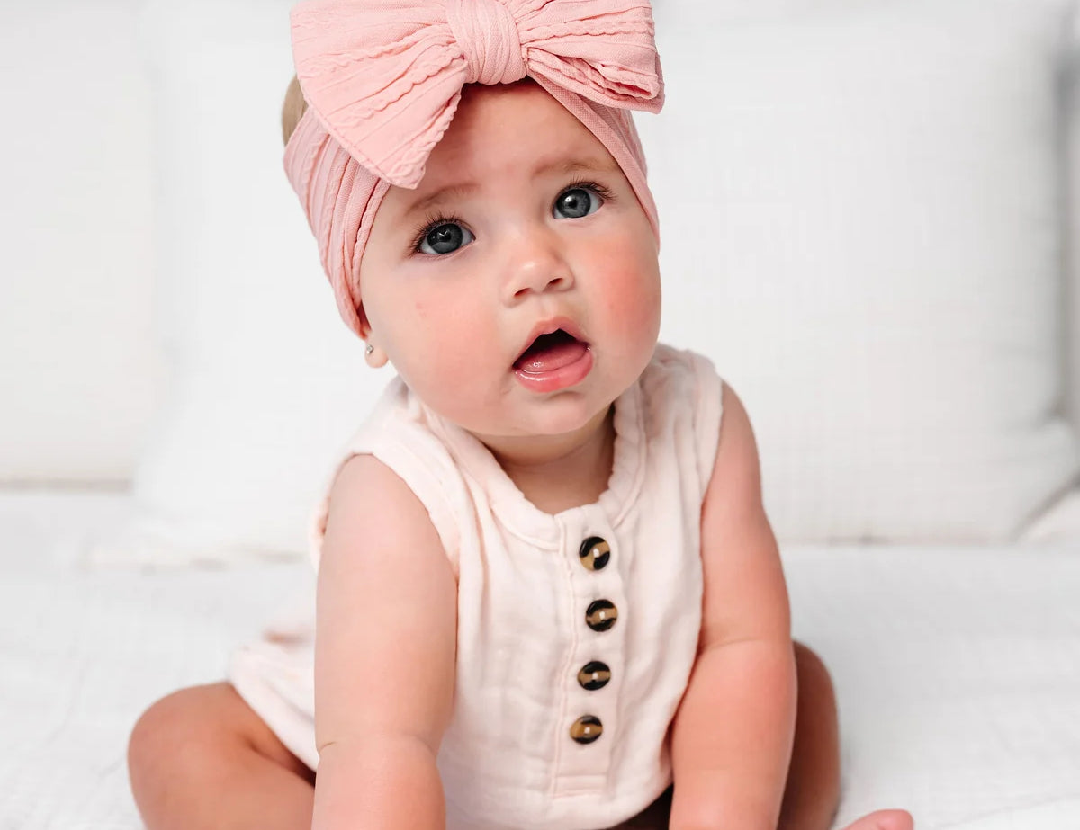 Baby in a blush romper wearing the Lou Lou & Company Cable Knit Headband in Rose