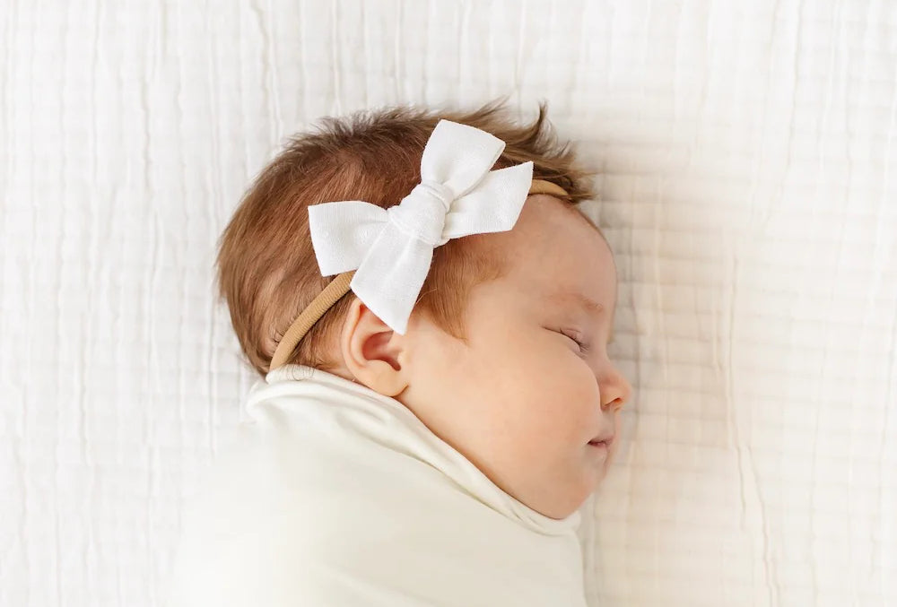 Sleeping newborn swaddled in white wearing the Lou Lou & Company Classic Bow in White