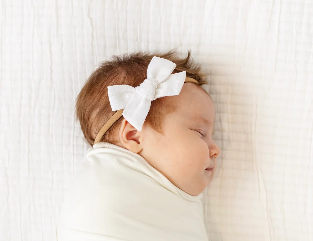 Sleeping newborn swaddled in white wearing the Lou Lou & Company Classic Bow in White