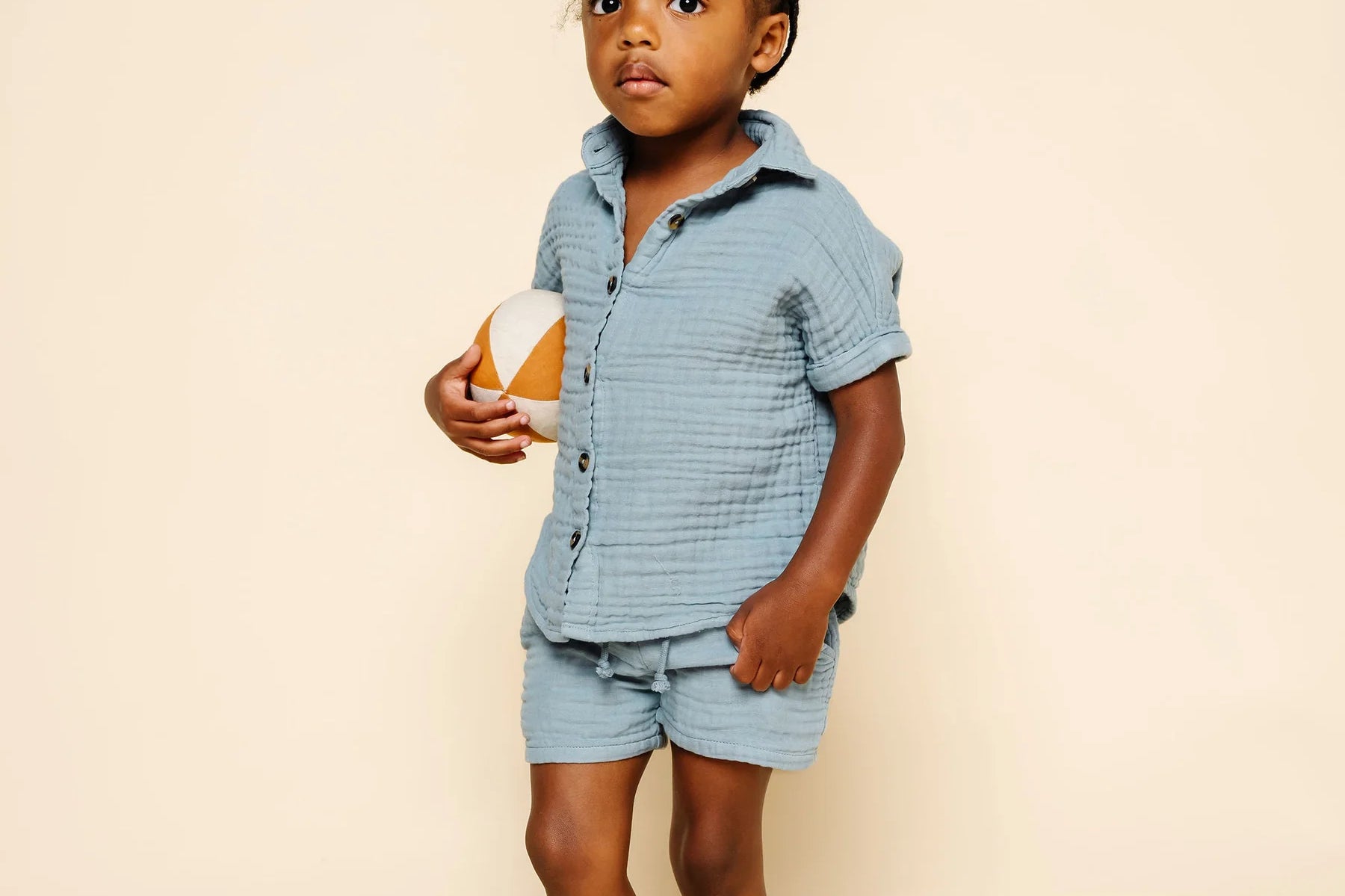 Toddler holding a ball wearing the Lou Lou & Company Cloud Muslin Shirt and Shorts in Steel
