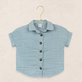 Lou Lou & Company Cloud Muslin Shirt in Steel, a soft blue button-front short-sleeve shirt on a hanger