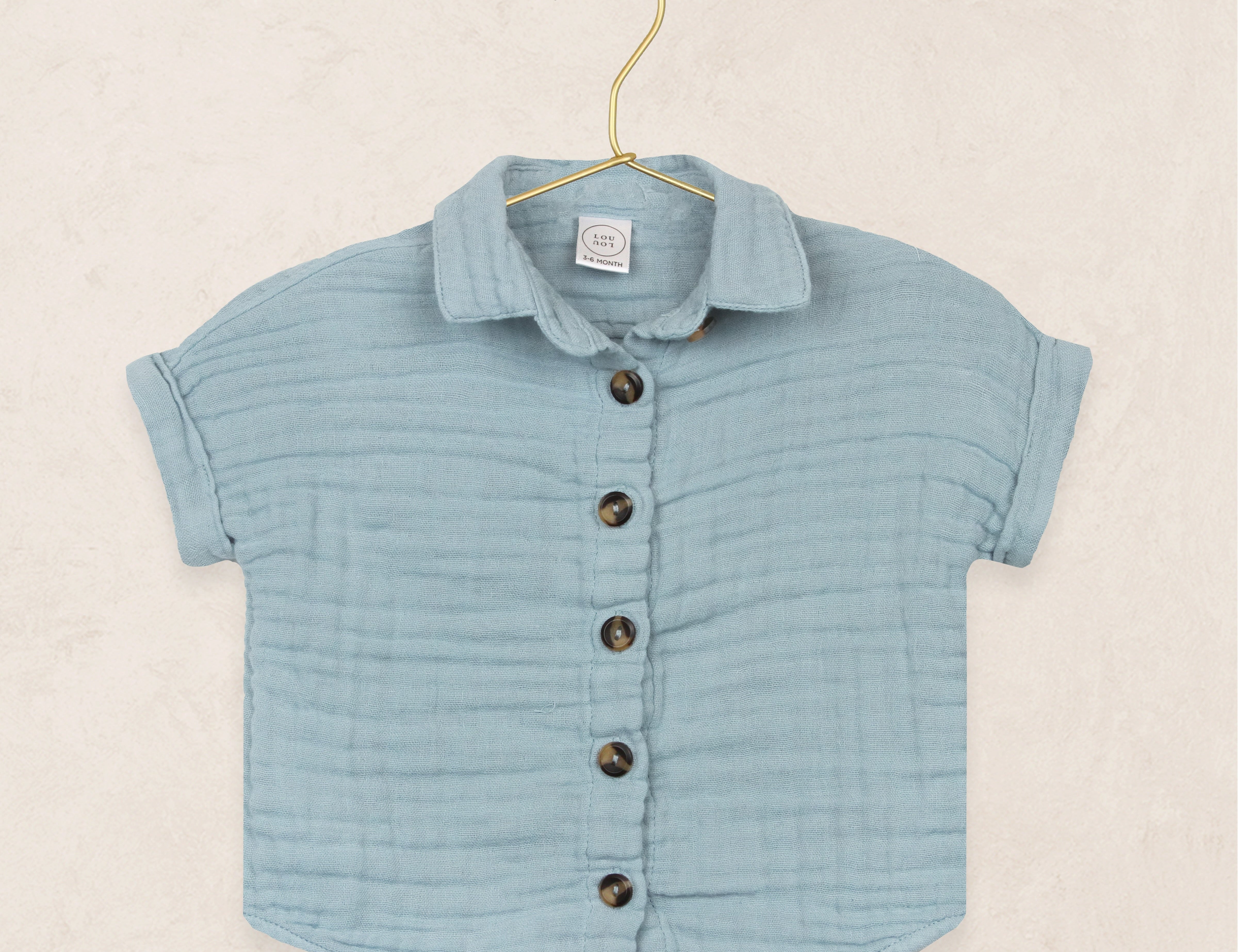Lou Lou & Company Cloud Muslin Shirt in Steel, a soft blue button-front short-sleeve shirt on a hanger