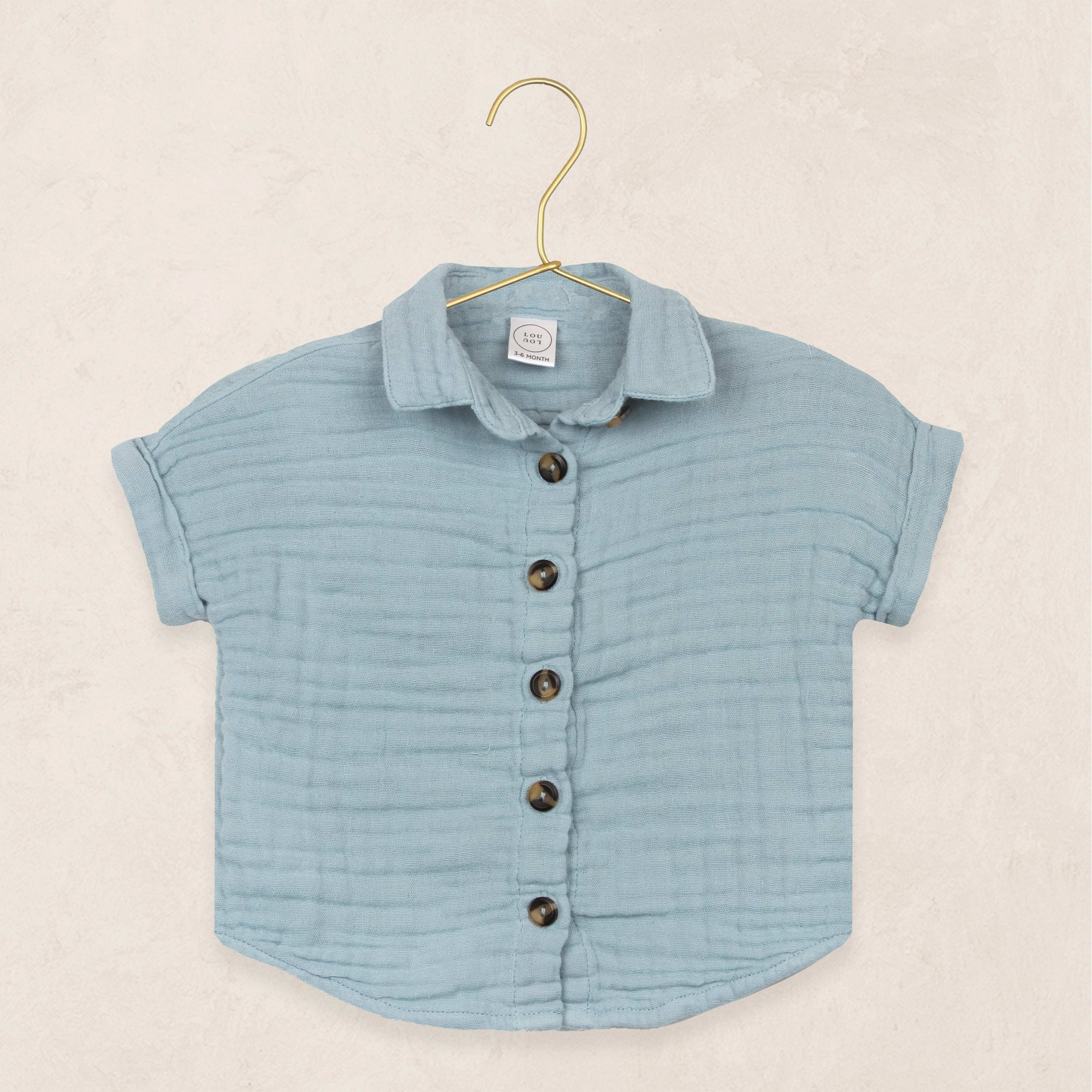Lou Lou & Company Cloud Muslin Shirt in Steel, a soft blue button-front short-sleeve shirt on a hanger