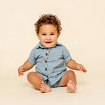 Smiling baby sitting in the Lou Lou & Company Cloud Muslin Shorts and Shirt in Steel