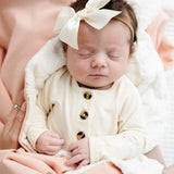 Newborn with a cream bow sleeping on the sherpa side of the Lou Lou & Company Cozy Blanket in Ballet Pink