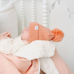 Newborn in a coral pom hat wrapped in the Lou Lou & Company Cozy Blanket in Ballet Pink