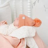 Newborn in a coral pom hat wrapped in the Lou Lou & Company Cozy Blanket in Ballet Pink