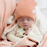 Sleeping newborn in a coral beanie snuggled in the Lou Lou & Company Cozy Blanket in Ballet Pink