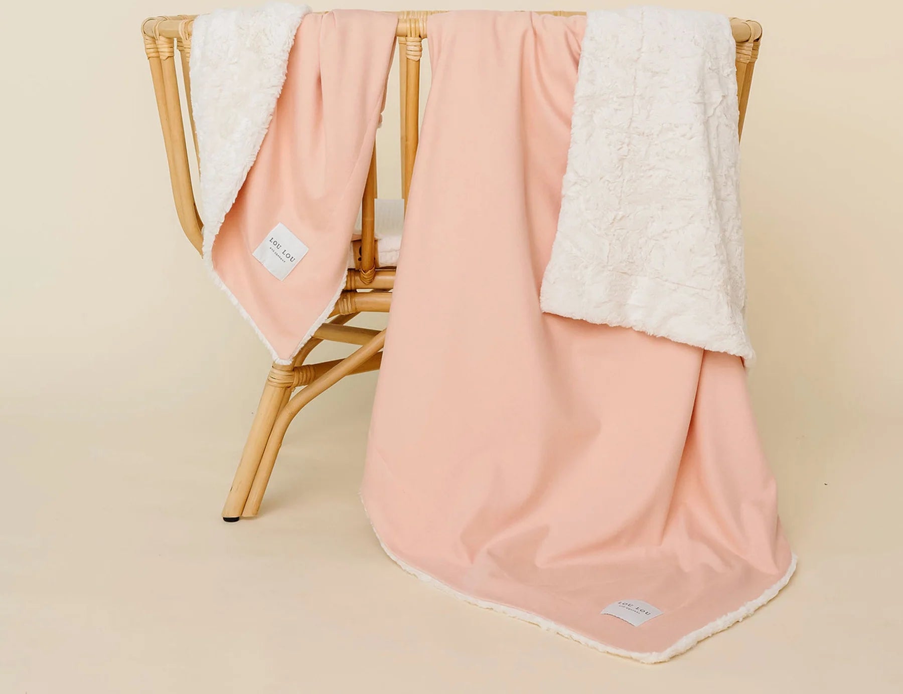 Lou Lou & Company Cozy Blanket in Ballet Pink draped over a rattan chair, showing the cream sherpa lining