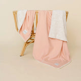 Lou Lou & Company Cozy Blanket in Ballet Pink draped over a rattan chair, showing the cream sherpa lining