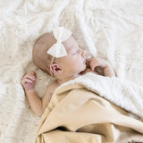 Newborn with a white bow sleeping under the Lou Lou & Company Cozy Blanket in Latte on sherpa
