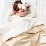 Newborn with a bow lying under the Lou Lou & Company Cozy Blanket in Latte