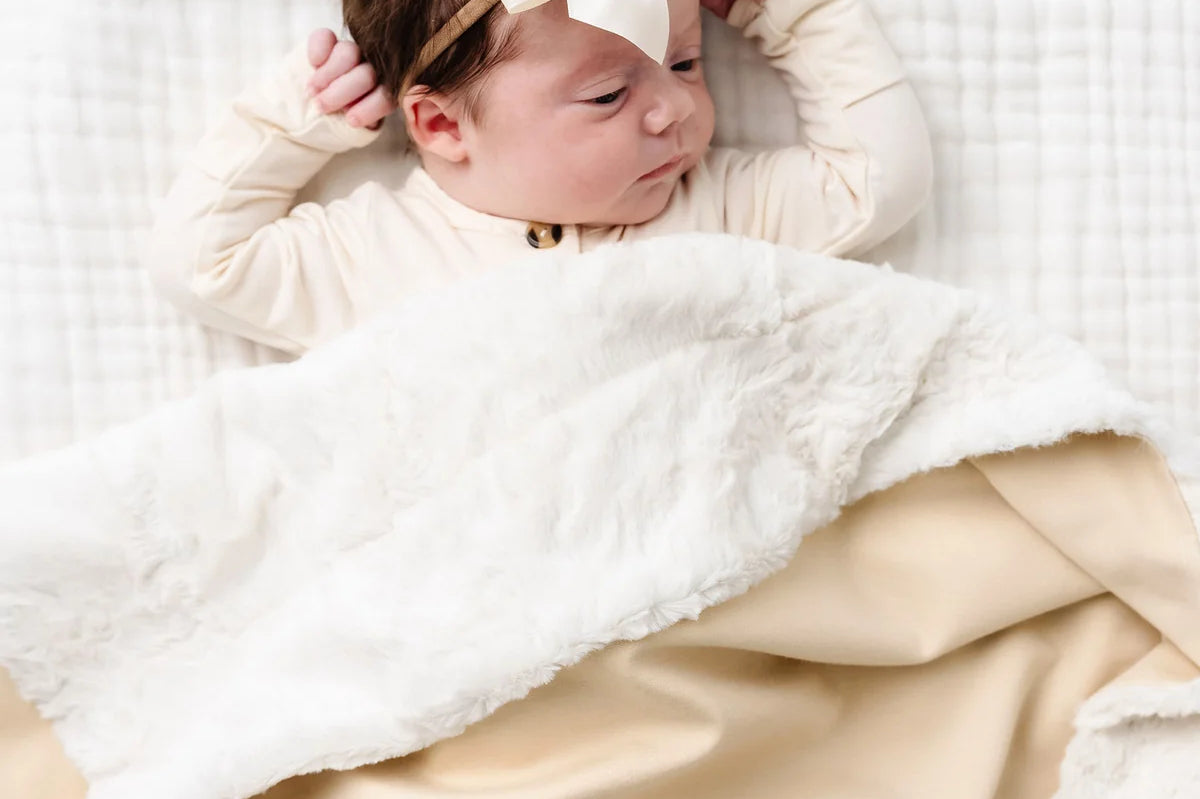 Newborn with a bow lying under the Lou Lou & Company Cozy Blanket in Latte