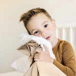 Toddler boy hugging the Lou Lou & Company Cozy Blanket in Latte with the sherpa side showing