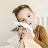 Toddler boy hugging the Lou Lou & Company Cozy Blanket in Latte with the sherpa side showing