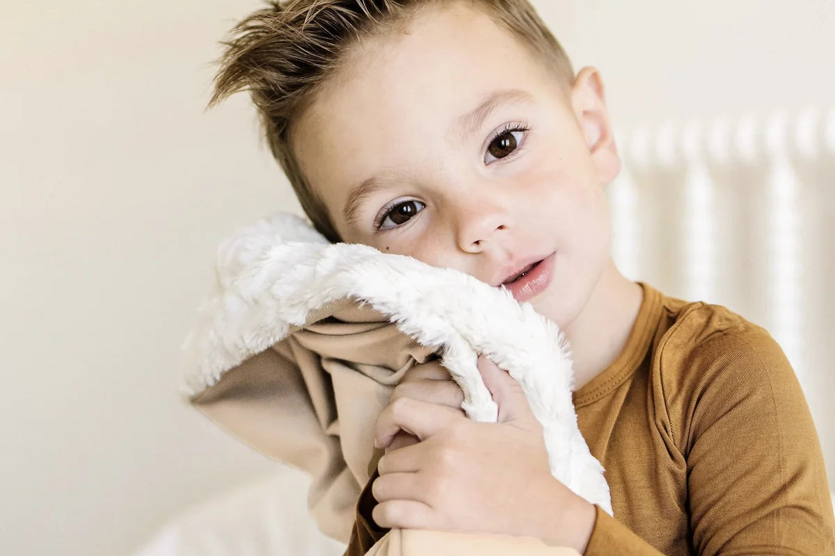 Toddler boy hugging the Lou Lou & Company Cozy Blanket in Latte with the sherpa side showing