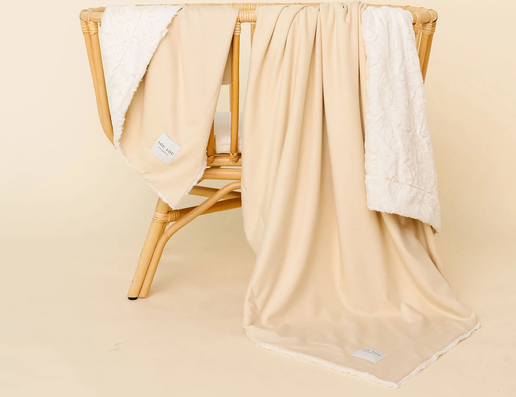 Lou Lou & Company Cozy Blanket in Latte draped over a rattan chair, showing the cream sherpa lining