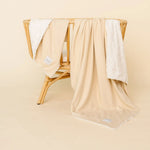 Lou Lou & Company Cozy Blanket in Latte draped over a rattan chair, showing the cream sherpa lining