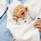 Yawning newborn in a white hat wrapped in the Lou Lou & Company Cozy Blanket in Steel blue