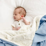 Newborn lying on the sherpa side of the Lou Lou & Company Cozy Blanket in Steel blue