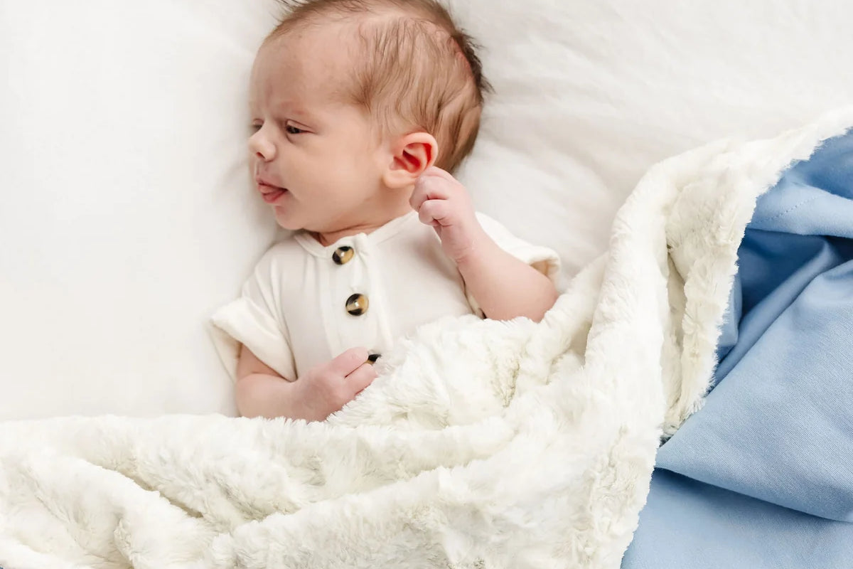 Newborn lying on the sherpa side of the Lou Lou & Company Cozy Blanket in Steel blue