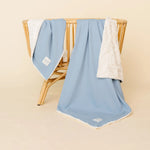 Lou Lou & Company Cozy Blanket in Steel blue draped over a rattan chair, showing the cream sherpa lining