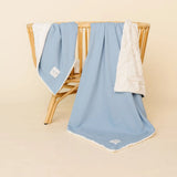 Lou Lou & Company Cozy Blanket in Steel blue draped over a rattan chair, showing the cream sherpa lining