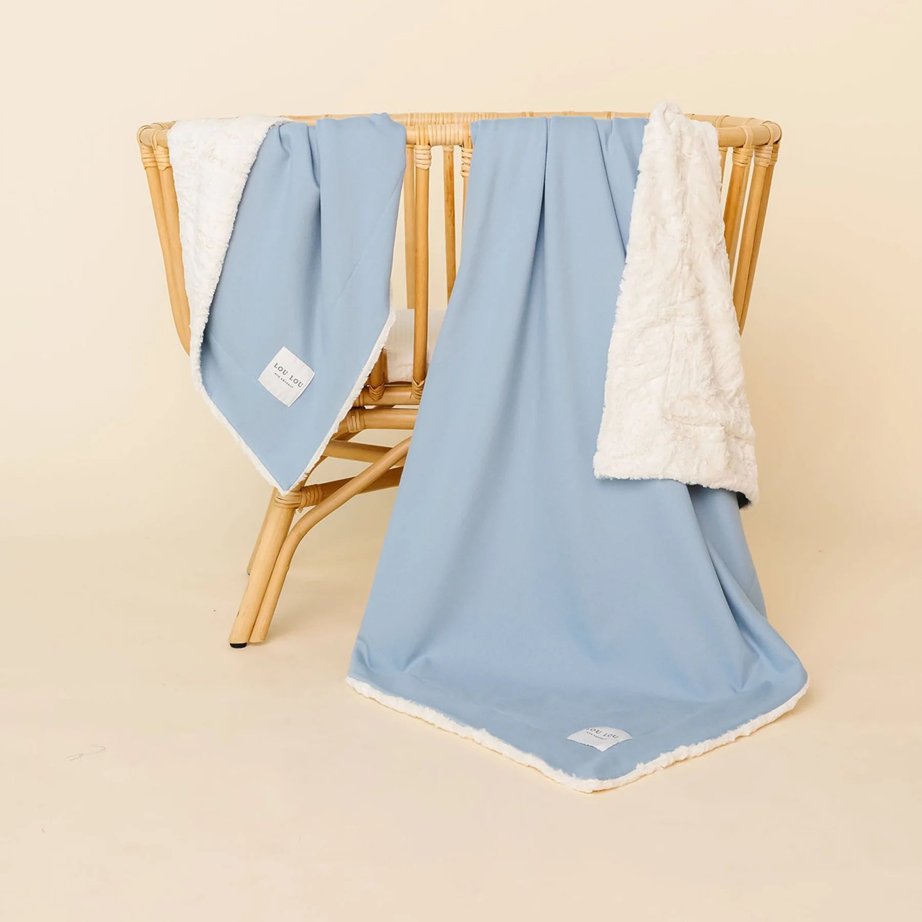Lou Lou & Company Cozy Blanket in Steel blue draped over a rattan chair, showing the cream sherpa lining