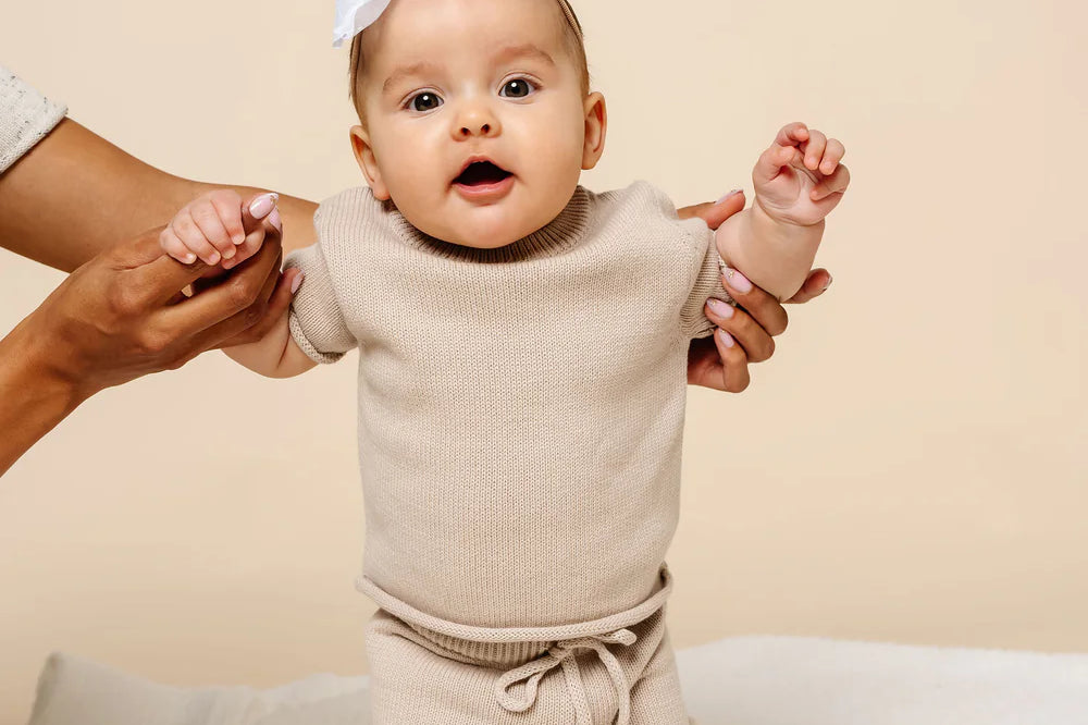 Baby with a white bow held up in the Lou Lou & Company Knit Tee and Shorts in Tan