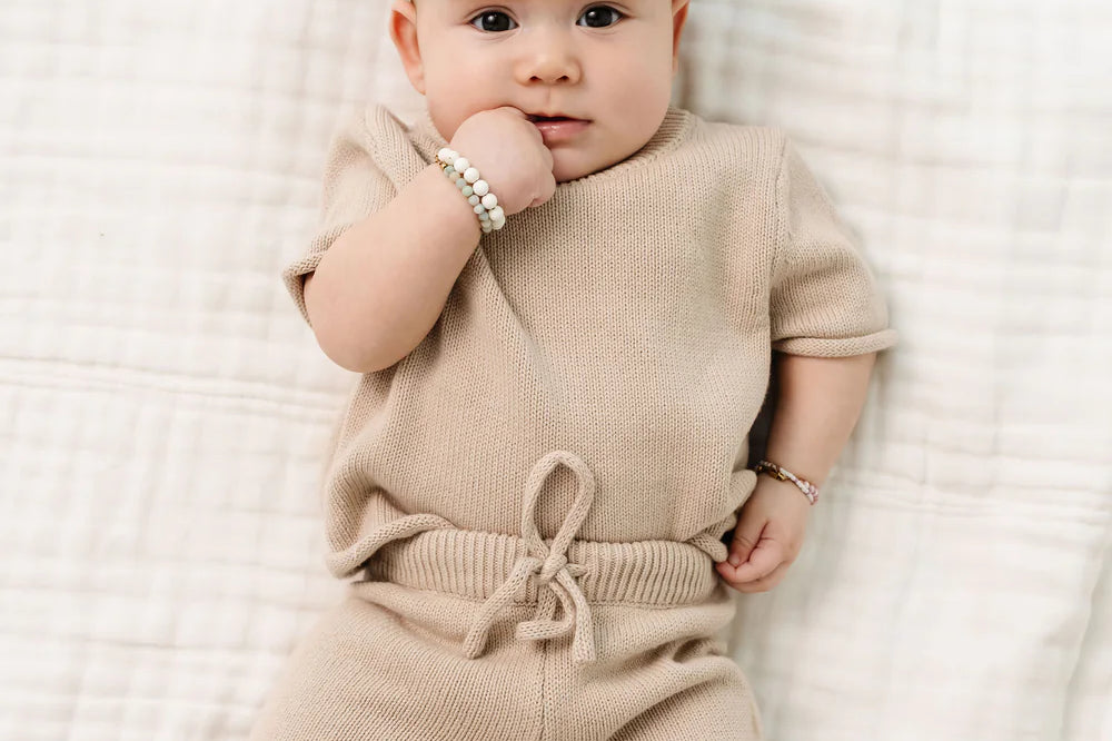 Baby with a white bow lying on a blanket in the Lou Lou & Company Knit Tee and Shorts in Tan