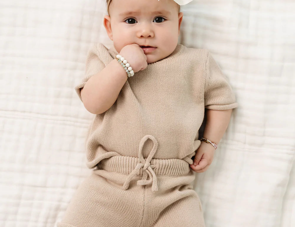 Baby with a white bow lying on a blanket in the Lou Lou & Company Knit Tee and Shorts in Tan