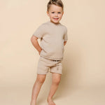 Smiling toddler boy standing in the Lou Lou & Company Knit Shorts and Tee in Tan