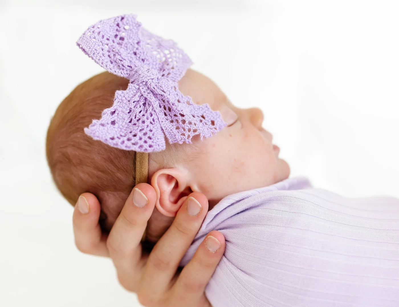Newborn swaddled in lavender wearing the Lou Lou & Company Lace Bow Headband in Lavender
