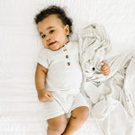 Baby lying on a white bed wearing the Lou Lou & Company Ribbed Romper in Stevie gray