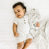 Baby lying on a white bed wearing the Lou Lou & Company Ribbed Romper in Stevie gray